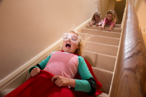 daredevil child comes down the stairs in a sleeping bag toboggan pushed by sisters
