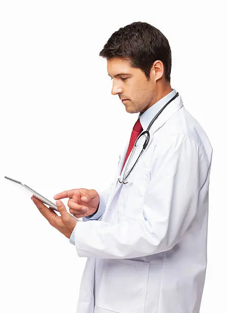 Side view of a serious young male doctor in lab coat using digital tablet. Vertical shot. Isolated on white.