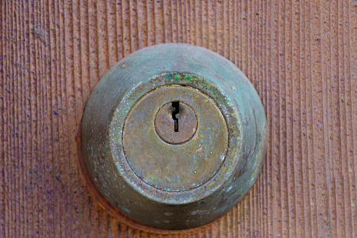 A close up image of a old and rusted metal door lock on a brownish-red wooden door.