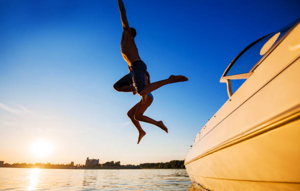 deux personnes sautant dans l'eau contre le ciel bleu. - cruise speed photos et images de collection