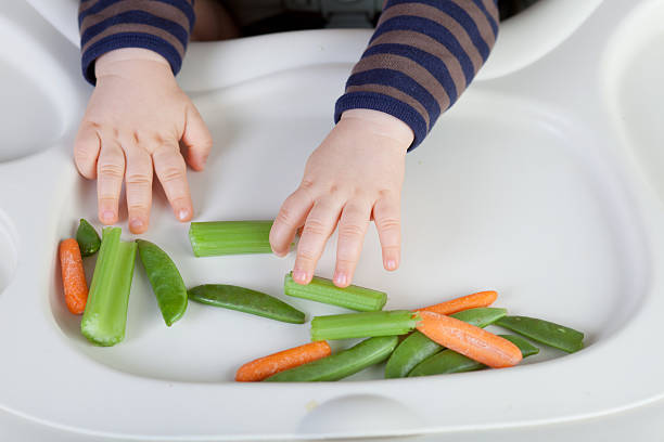 Hands of one year boy reaching for healthy veggies on his high chair.