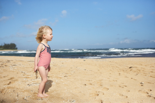 Rear view of a beautiful little girl walking along the beach. Vertically framed shot.