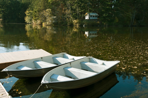 Two rowboats moored to shore and summer cabin on shallow lake in autumn