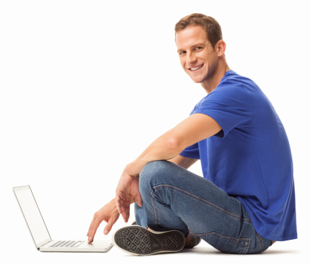 Portrait of handsome young man in casual wear sitting cross-legged on floor with laptop. Horizontal shot. Isolated on white.