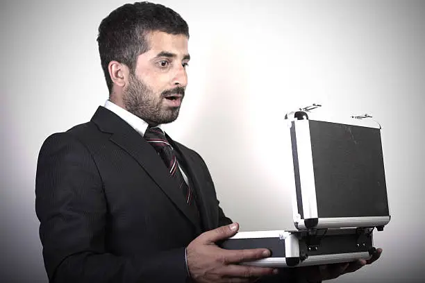 Surprised young businessman looking into his hardcase. Horizontal studio shot.