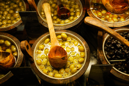 Different kinds of pickled olives in wooden pails  under the counter glass