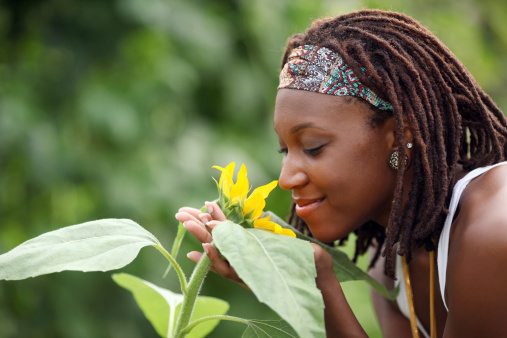 Young woman smelling a flower from a garden while having a happy expression.