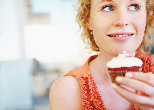 A pretty young woman holding a cupcake and looking away happily