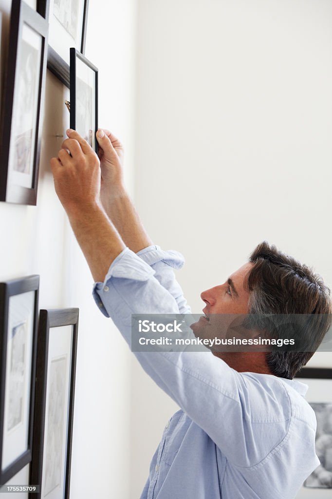 Man Hanging Picture Frames On Wall At Home "Man Hanging Picture Frames On Wall At Home, Side View Of Man" Hanging Stock Photo