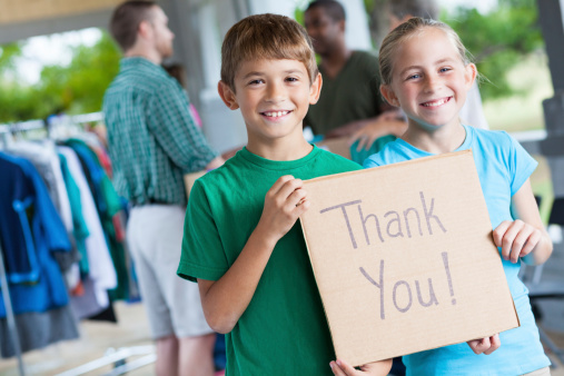 Children holding Thank You sign at donation center or yard sale.
