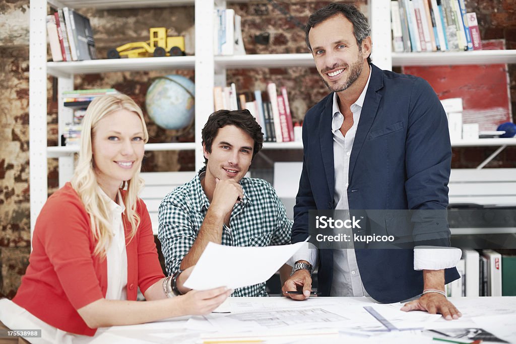 Designing the future of architecture Three attractive architects around a table smiling at the camera while holding a piece of paper Adult Stock Photo