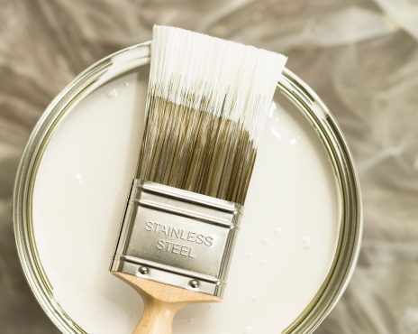 Home decoration: a brush dipped in white paint over a protective sheet.