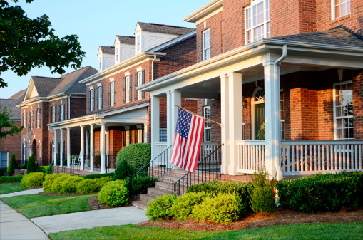 A row of traditional brick homes with an American Flag hanging from the front of the first house. Beautiful light as the sun is setting in the West.