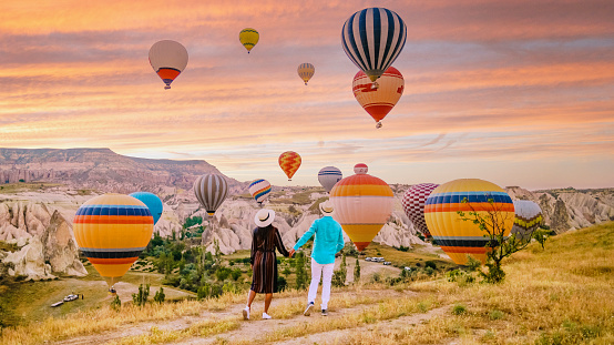 Cappadocia Turkey during sunrise, a mature couple of men and woman on vacation in the hills of Goreme Cappadocia Turkey, men and woman looking sunrise with hot air balloons in Kapadokya Turkey