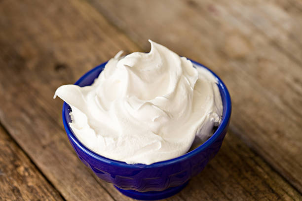 A high angle close up shot of a blue bowl  full of white whipped cream. Shot on an old grungy outdoors wooden  table.