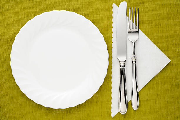 istock White plate with silver knife and fork on green tablecloth 175540492