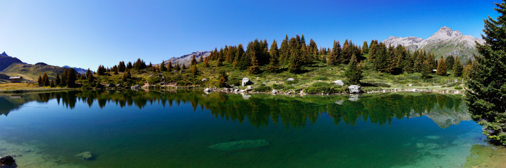 The Monte Rosa peaks are reflected the lake called Blue Lake, on a sunny, crystal-clear autumn morning. The larch trees have already changed their colors to warmer autumn hues.