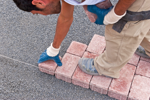 Paver setting paving blocks on grit along a guideline for accuracy.
