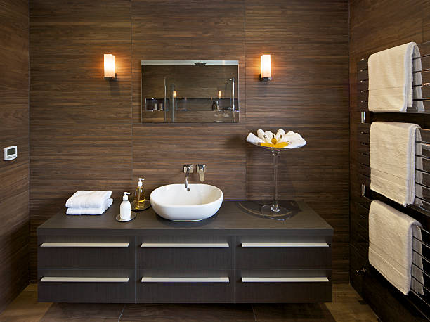 brown tiled guests bathroom a section of a large guest's bathroom in a luxury new home with a large cabinet with drawers and a modern white basin on top. The walls are lined with wood-design ceramic tiles and the floor has large section tiles to match. A modern chrome radiator with white towels is on the right. Toiletries and hand towels have been used to dress the bathroom.Looking for a Bathroom image Then please see my other Bathrooms and related inages by clicking on the Lightbox link below...A>AA>A faux wood stock pictures, royalty-free photos & images