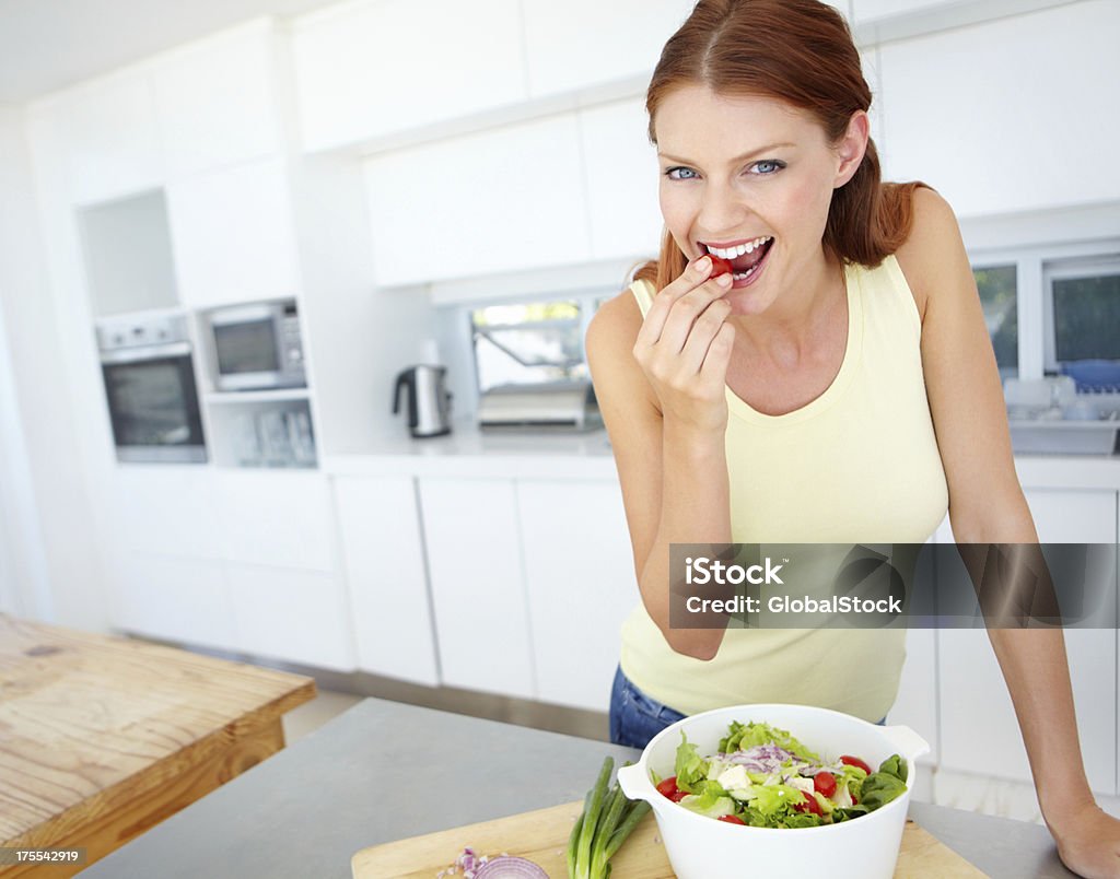 Sneaking a tomato before dinner Portrait of an attractive young woman eating a baby tomato in the kitchen 20-29 Years Stock Photo