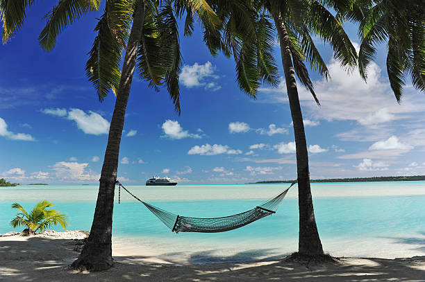 Arrival in Paradise A cruise ship appears on the horizon of a tropical turquoise lagoon - with a hammock in semi silhouette, shaded by palm trees atoll photos stock pictures, royalty-free photos & images