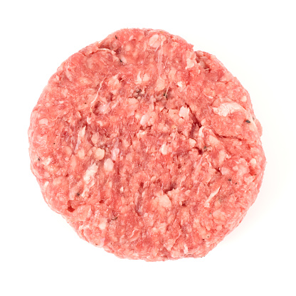 Uncooked healthy burgers made of beef and pork on the white plate served with heads of garlic, peppercorns on a white table