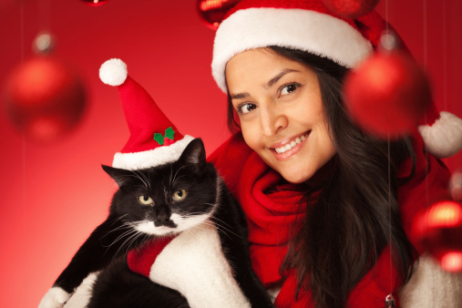 Subject: A Happy young woman celebrating Christmas with a Christmas gift pet cat in a red background and Christmas decorations.