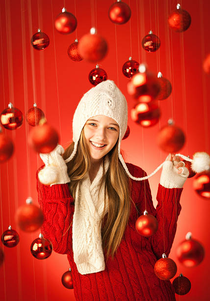 Subject: A Happy young teen model in winter fashion, celebrating Christmas in a red background with Christmas decorations.