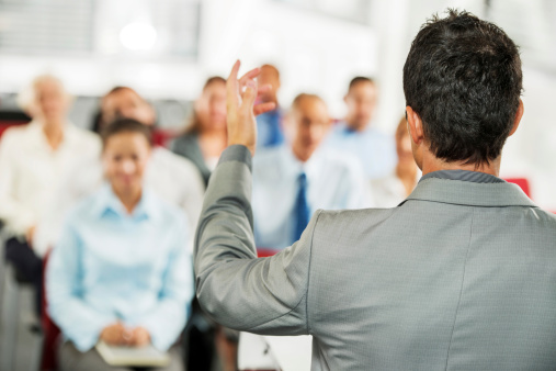 Male presenter giving a public speech in front of the business audience.