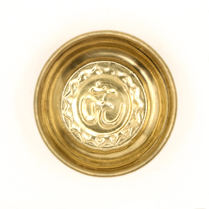 a traditional golden prayer bowl with an antique hindu om symbol carved inside the plate isolated in a white background