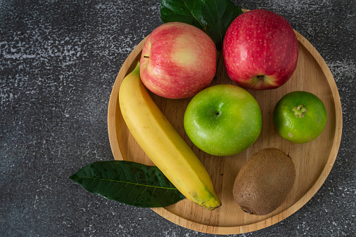Red and green apples, kiwi and bananas in a plate on a gray background.