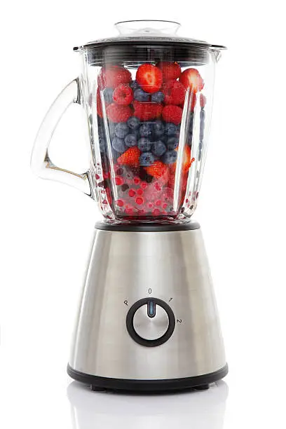 "Blender filled with Berries -  a fruit shake waiting to happen - Strawberries & BlueberriesIsolated on white background, reflection on the floor."