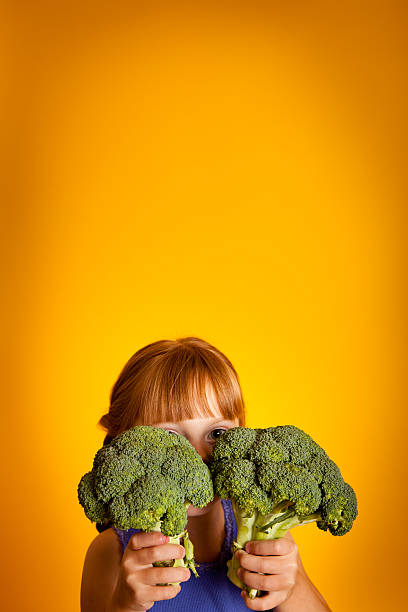 istock Little Girl Peeking Out From Behind Broccoli 175547365