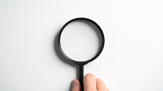 Hand holding magnifying glass isolated on white tabletop background.