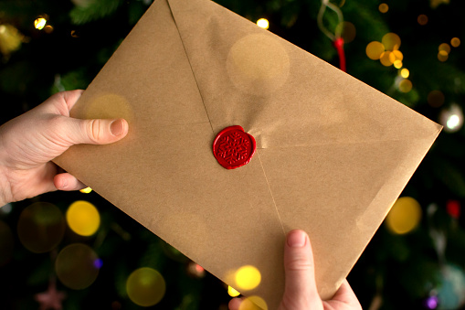 A child holds in his hands an envelope with wishes from Santa Claus. Wish list for Santa Claus inside