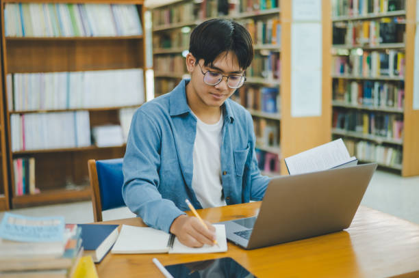 istock Male college students are working on laptops and searching for books to study, make reports, find useful information in college room. Concept of reading, learning and intelligence. 1755542852