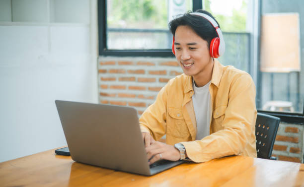 istock Student using a laptop in a cafe while wearing headphones, learning and searching the internet, and making a video call. 1755545212