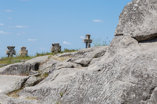 Old stone crosses as tombstones on the medieval Cossack graves on the hill top with the rock on a foreground, selective focus. Pidkamin village, Ukraine