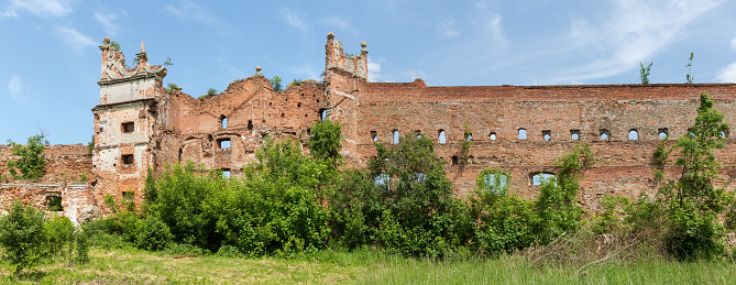 Ruins of the brick defense tower and wall of the mediaeval castle overgrown with different shrubs in Stare Selo village, Ukraine. Panoramic view from the inner courtyard side