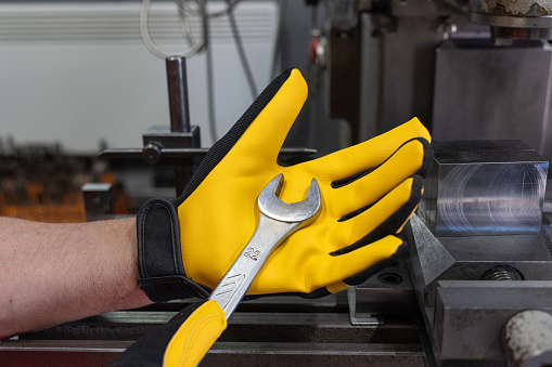 Wrench in male hands in yellow protective gloves against the background of a machine tool.. High quality photo