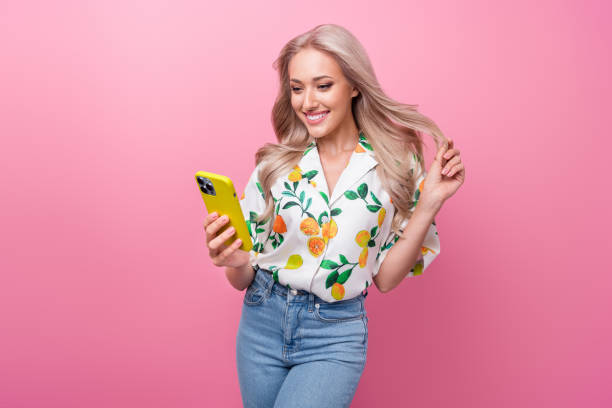 istock Photo of nice girlfriend touch her blonde curls browsing phone makeup website order conditioner for hair isolated on pink color background 1755608826