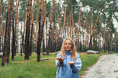 Overjoyed blonde woman in blue raincoat enjoying silence natural green environment woods in the forest. Happy emotion open arms outdoors in rainy weather. Unity with nature physical wellbeing