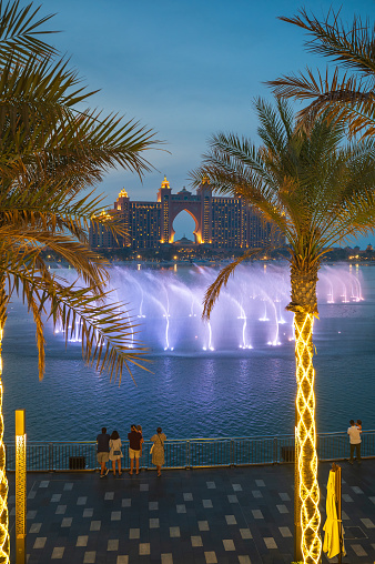 Dubai, United Arab Emirates - April 22, 2022: Music fountain show near Atlantis The palm hotel reflected in the seaside with fountain show setup on artificial palm island in Dubai, UAE at blue hour. Famous travel and leisure spot in the emirate