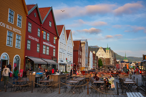 Bergen, Norway - June 23, 2023: Patrons enjoy a beverage at an outdoor bar on a deck outside Bryggen, a series of Hanseatic heritage commercial buildings lining up the east side of the Vågen harbor.