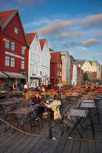 Bergen, Norway - June 23, 2023: Patrons enjoy a beverage at an outdoor bar on a deck outside Bryggen, a series of Hanseatic heritage commercial buildings lining up the east side of the Vågen harbor.