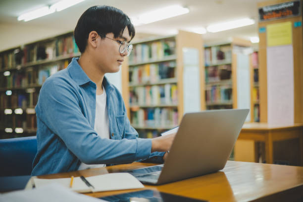 istock Male college students are working on laptops and searching for books to study, make reports, find useful information in college room. Concept of reading, learning and intelligence. 1755629550