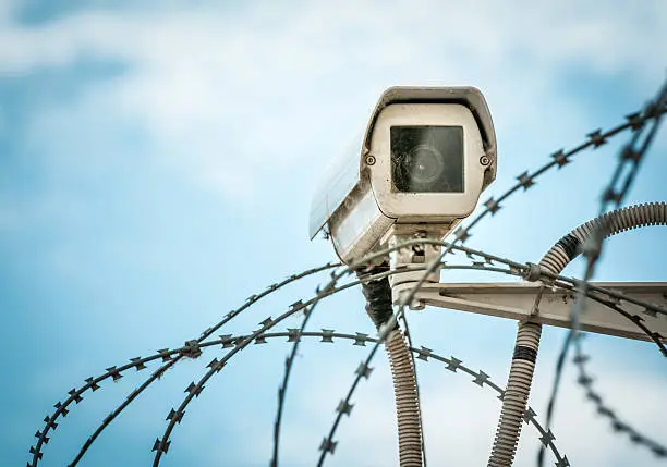 Photo of Observation camera and barbwire on blue sky.