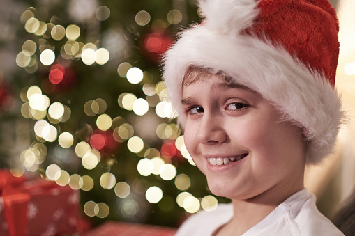 Funny portrait of a boy at Christmas. A teenager in a Santa hat near a Christmas tree.