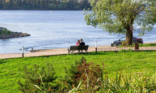 Romantic couple in love, sitting on riverside bench, sharing tender moment by the water. Love by river.