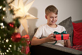 Joyful child holding Christmas gift with interest. Boxing day. Bokeh lights and decorations.